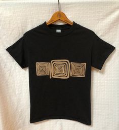 a black t - shirt with gold squares on it hanging from a wooden hanger