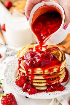 a stack of pancakes with strawberry syrup being drizzled over them on a white plate