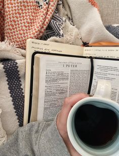 a person holding a cup of coffee and reading a book with an open book on it