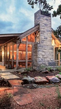 a small cabin is lit up at night in the woods with rocks and trees surrounding it