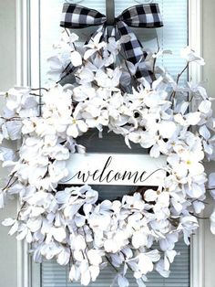 a white wreath with black and white flowers on the front door is decorated with a welcome sign