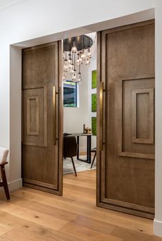 an open door leading to a dining room and living room with wood floors, chandelier and table