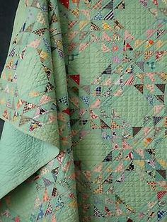 a green quilt with many different designs on it and the bottom half is folded up