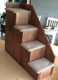 a set of stairs made out of cardboard with carpet on the bottom, and two white chairs in the background