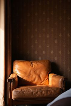 a brown leather chair sitting in front of a window next to a wallpapered wall