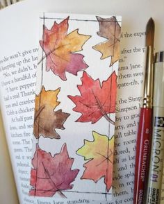 an open book with watercolor leaves on it and two pens sitting next to it