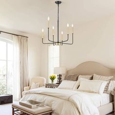 a bedroom with a large bed, chandelier and two chairs in front of the window