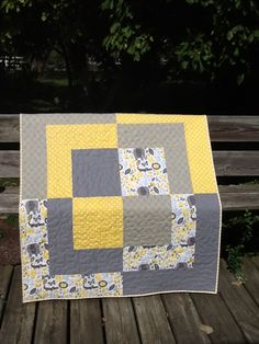 a gray and yellow quilt sitting on top of a wooden bench