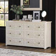 a white dresser sitting in front of a window next to a mirror and framed pictures