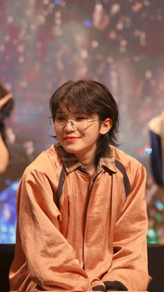 a woman sitting on top of a wooden bench next to a man wearing glasses and an orange shirt