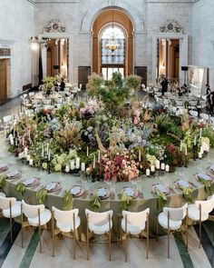 a circular table with chairs and flowers on it in a large room filled with people