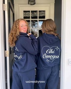 two women standing in front of a door wearing matching blue sweat suits with white writing on them