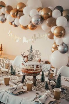 a table topped with a cake covered in frosting next to balloons and christmas trees