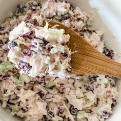 a wooden spoon in a white bowl filled with coleslaw and cranberries