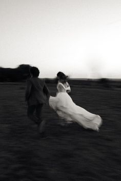 black and white photograph of two people running in a field with one person wearing a dress