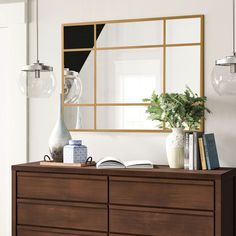 a dresser with books and vases on it in front of a large framed mirror