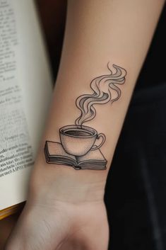 a woman's arm with a cup of coffee and book tattoo on her wrist