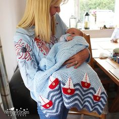 a woman holding a baby wrapped in a blue knitted blanket with boats on it