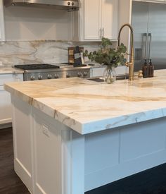 a kitchen with marble counter tops and stainless steel oven hoods, white cabinets and an island in the middle