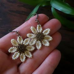 a pair of white beaded earrings on a person's hand next to a plant