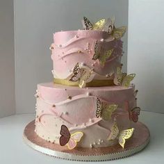 a three tiered cake with pink frosting and gold butterflies