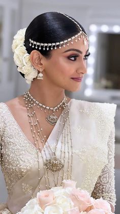 a woman in a bridal gown holding a bouquet of flowers and wearing pearls on her head