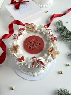 a white cake with red ribbon around it on a table next to some christmas decorations