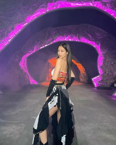 a woman in black and white outfit posing for the camera with purple lighting behind her