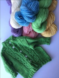 several skeins of yarn next to a green knitted baby's sweater