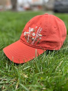 a red baseball cap with daisies on it laying in the grass near a house