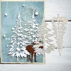 a christmas card with a moose and pine trees in the snow, on a white wooden background