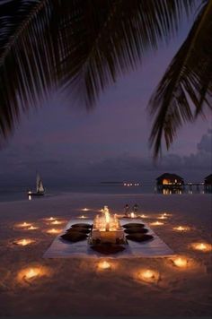 a table set up on the beach with lit candles in front of it at night