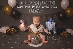 a baby sitting on the floor next to some balloons and star wars decorations in front of a backdrop