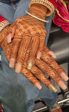 a woman's hands with hennap and gold glitters on them, sitting in