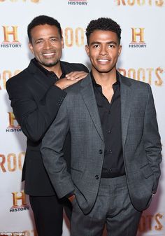 two men standing next to each other in front of a sign that says roots on it