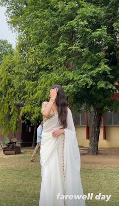 a woman in a white sari standing on the grass with her hands behind her head