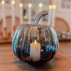 a small glass pumpkin with a lit candle in it's center on a wooden table