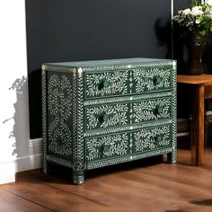 a green and white chest of drawers sitting on top of a wooden floor next to a table