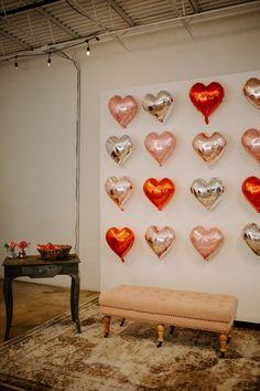 there are many heart shaped balloons hanging on the wall next to a bench and table