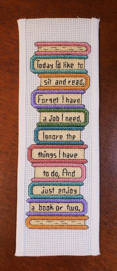 a cross - stitch bookmark with words on it sitting on top of a wooden table