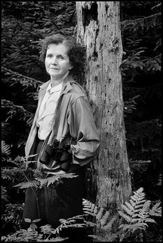 a woman standing next to a tree in the woods