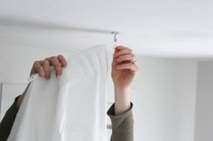 a person holding up a piece of white cloth to hang it on the wall above their head