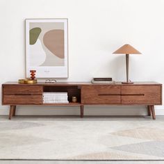 a modern wooden sideboard with two lamps on top and a painting hanging above it