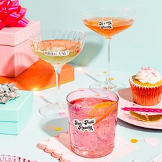 two glasses filled with drinks sitting on top of a table next to cupcakes