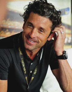 a man with curly hair is smiling and talking on the phone while wearing a black shirt