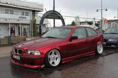 a red car parked in front of a building on a wet street with other cars behind it