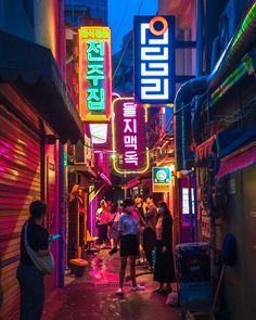 people are standing in an alley way with neon signs on the buildings behind them and one person is using his cell phone