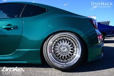 a green sports car with chrome rims parked in a parking lot next to other cars