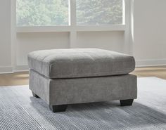 a large gray ottoman sitting on top of a rug in front of a white window