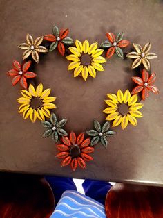 a heart made out of plastic flowers on a wooden table next to a blue vase